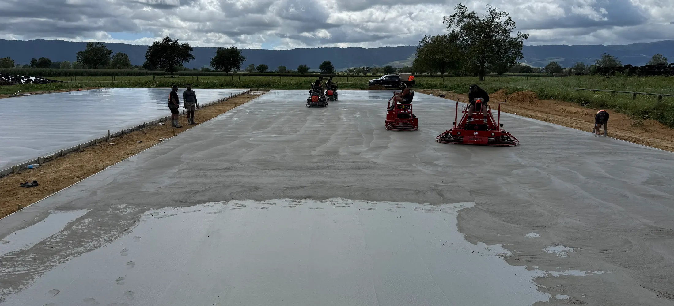 Ride-on power trowels working a large freshly floated concrete slab in open farmland