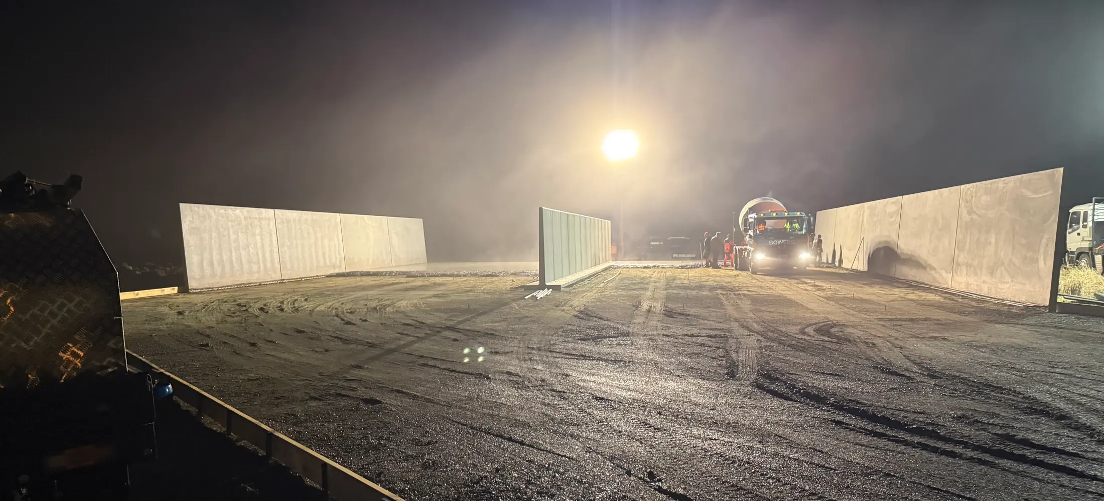 Precast concrete panel walls standing in the dust and floodlight during a night shift