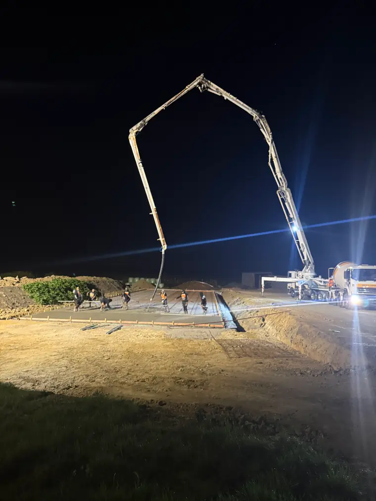 Concrete boom pump reaching over a bank to a night pour on the flat below