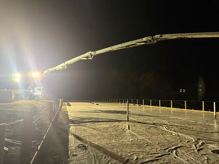 Boom pump placing concrete across a floodlit slab in the early hours of the morning