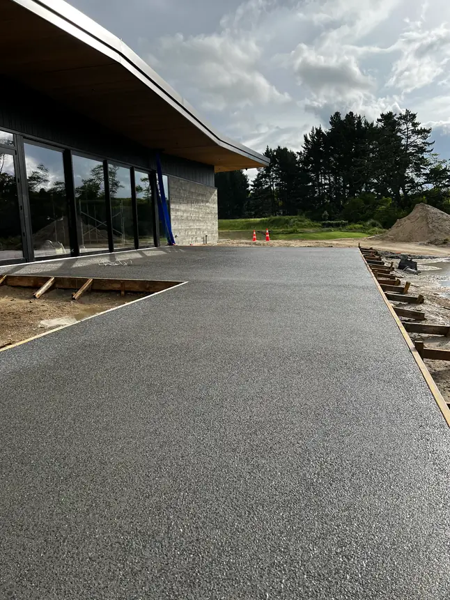 Charcoal exposed aggregate concrete driveway laid the length of a modern building