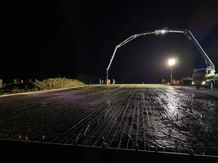 Reinforcing mesh and chairs laid out across a large slab, lit by floodlight before a night pour