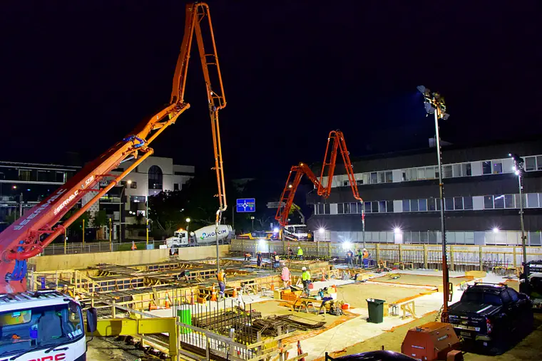 Two concrete pump booms lit up over a commercial pour running through the night in town