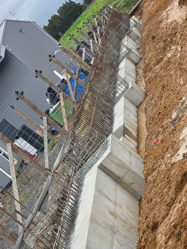 Steel reinforcing standing in a boxed retaining wall alongside a commercial building