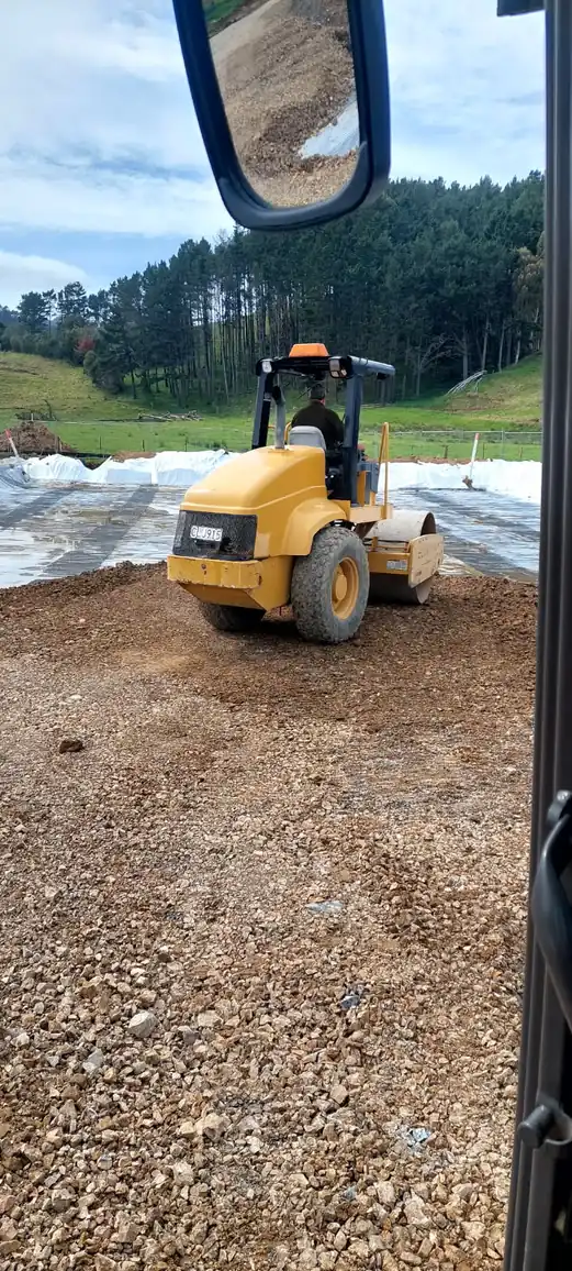 Roller compacting basecourse over geotextile, seen from the cab of the truck alongside