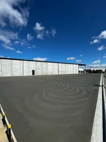 Decorative swirl finish troweled into a freshly placed concrete apron outside a large tilt-panel shed